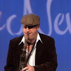 A man in brown jacket and hat playing saxophone.