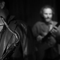 A man with a saxophone and another man playing an instrument.