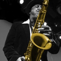 A man in black jacket holding a saxophone.